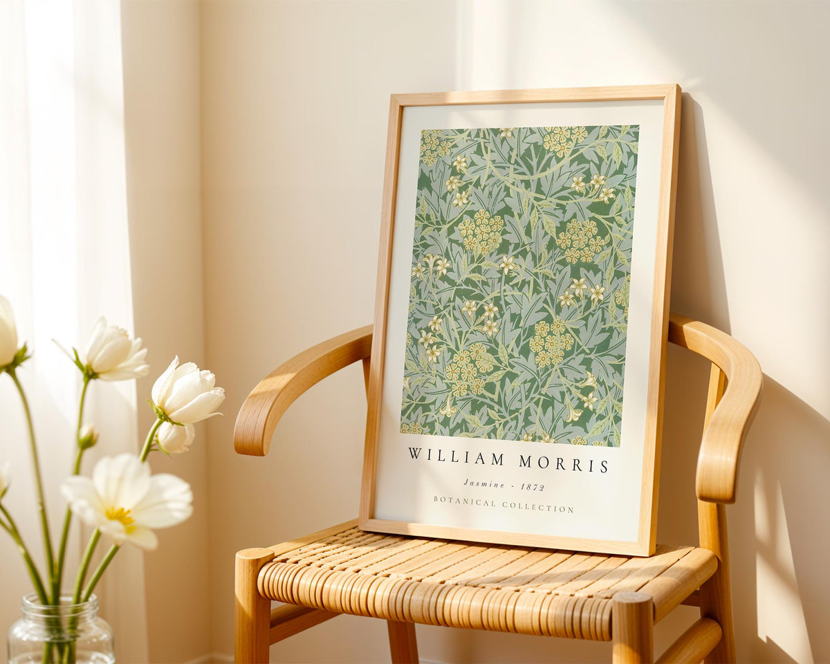 A framed botanical print titled "William Morris" is displayed on a wooden chair, with a vase of white flowers to the left.