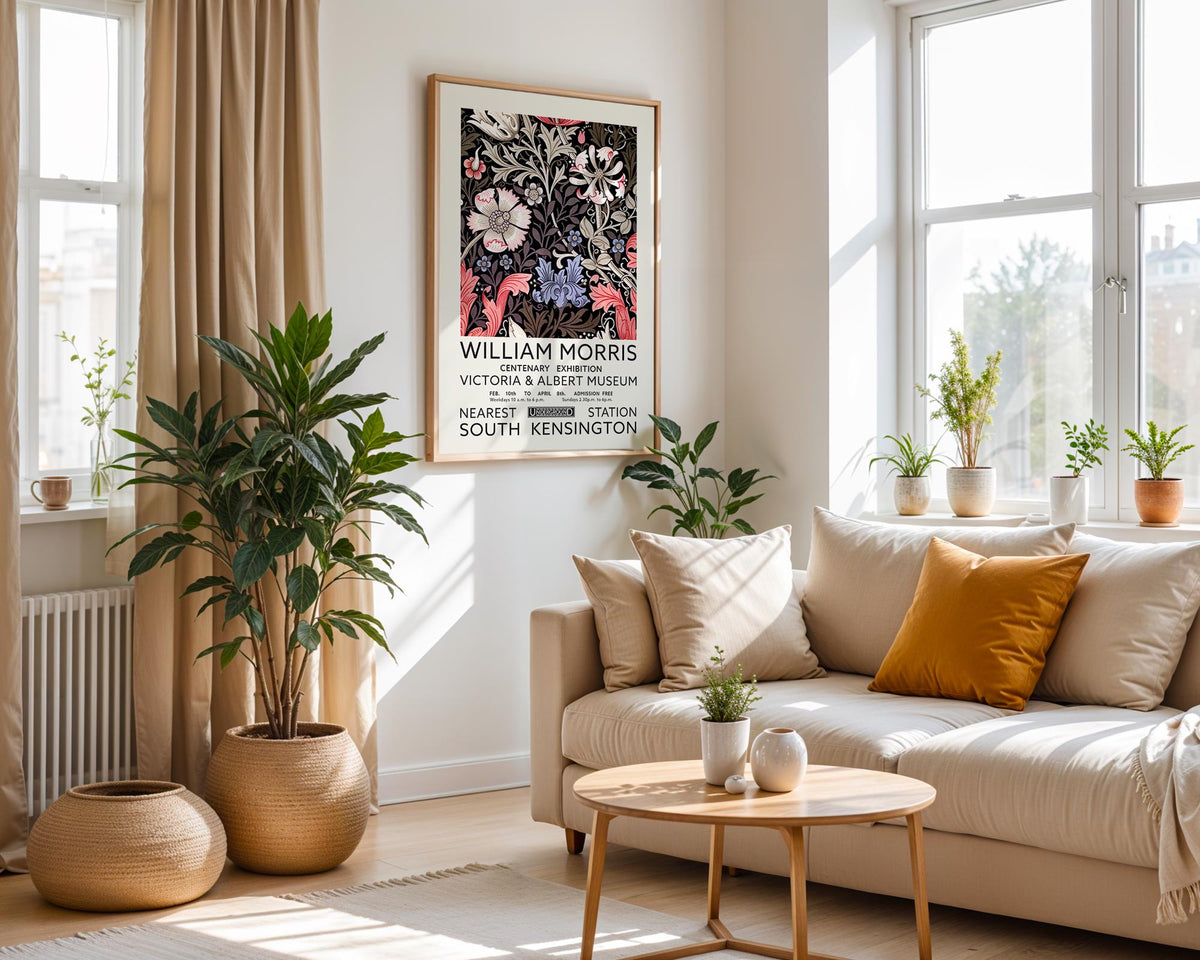 A cozy living room with a large window, a beige sofa, a coffee table, and several potted plants. A framed poster of William Morris hangs on the wall, and the room is decorated with various plants and other decorative items.