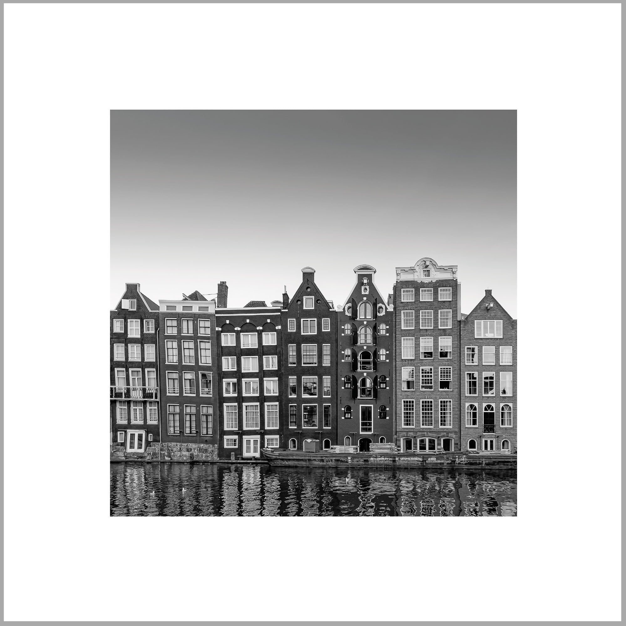 A row of tall, narrow buildings with steep roofs along the waterfront, reflecting in the water.