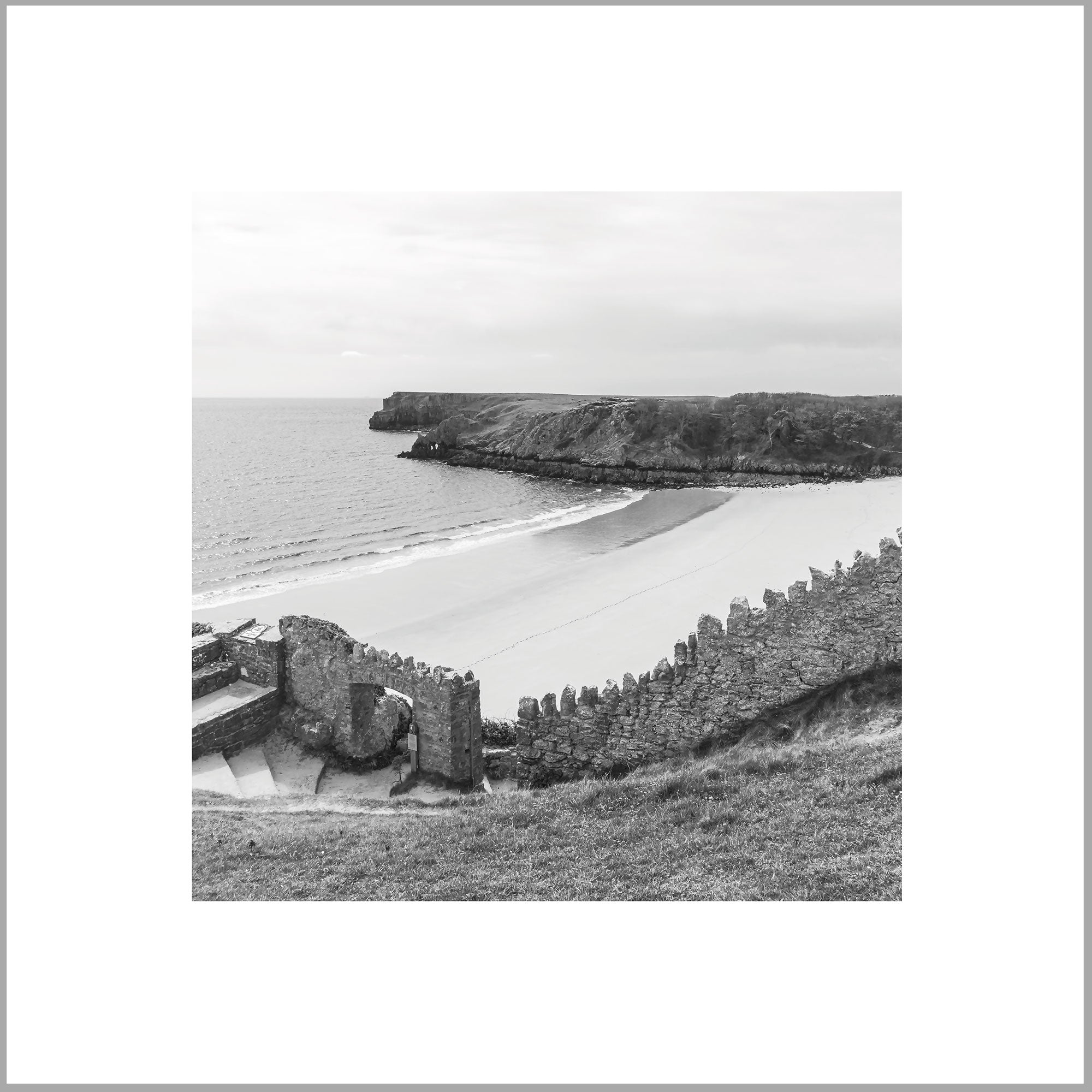 A black and white image depicting a coastal landscape with a rocky cliff, a sandy beach, and a body of water in the distance.