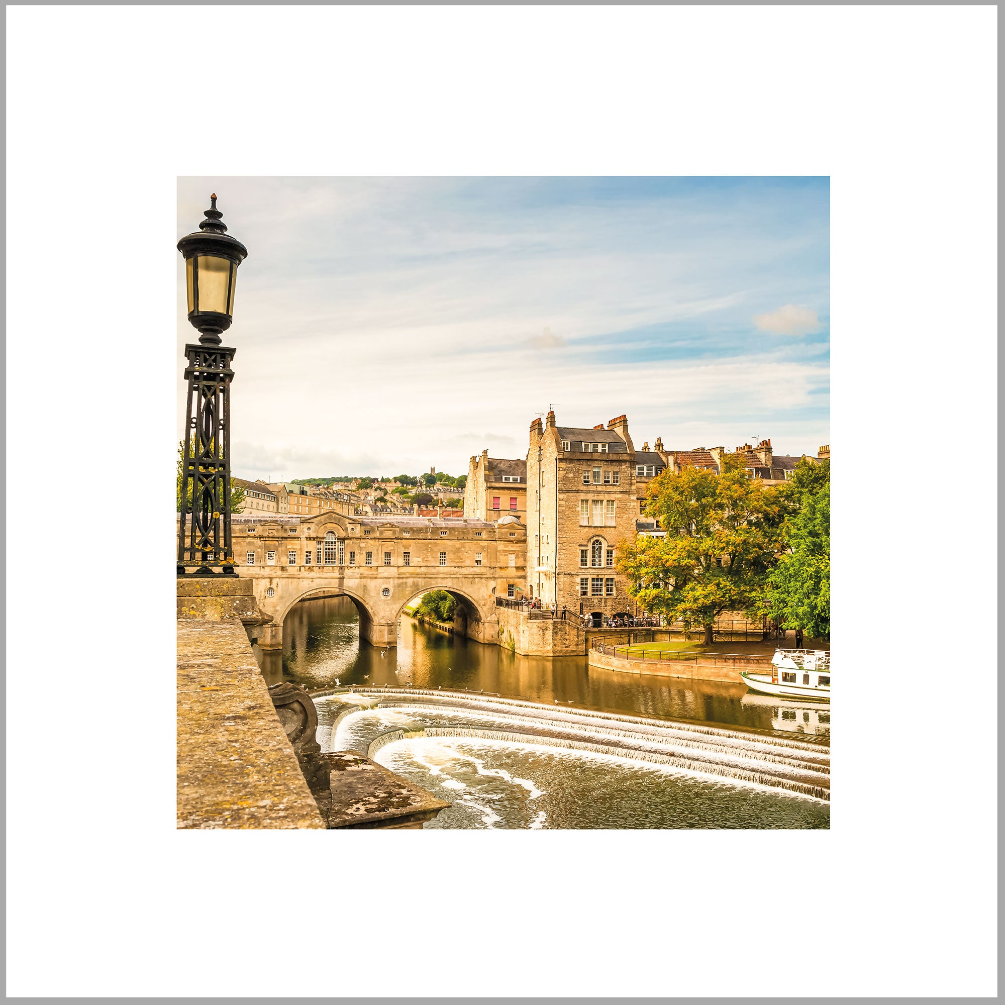 a picturesque scene of a stone bridge spanning a river, with a castle-like building in the background. The bridge is surrounded by lush greenery, and a boat can be seen on the river. The sky is clear blue with some clouds, creating a serene atmosphere.