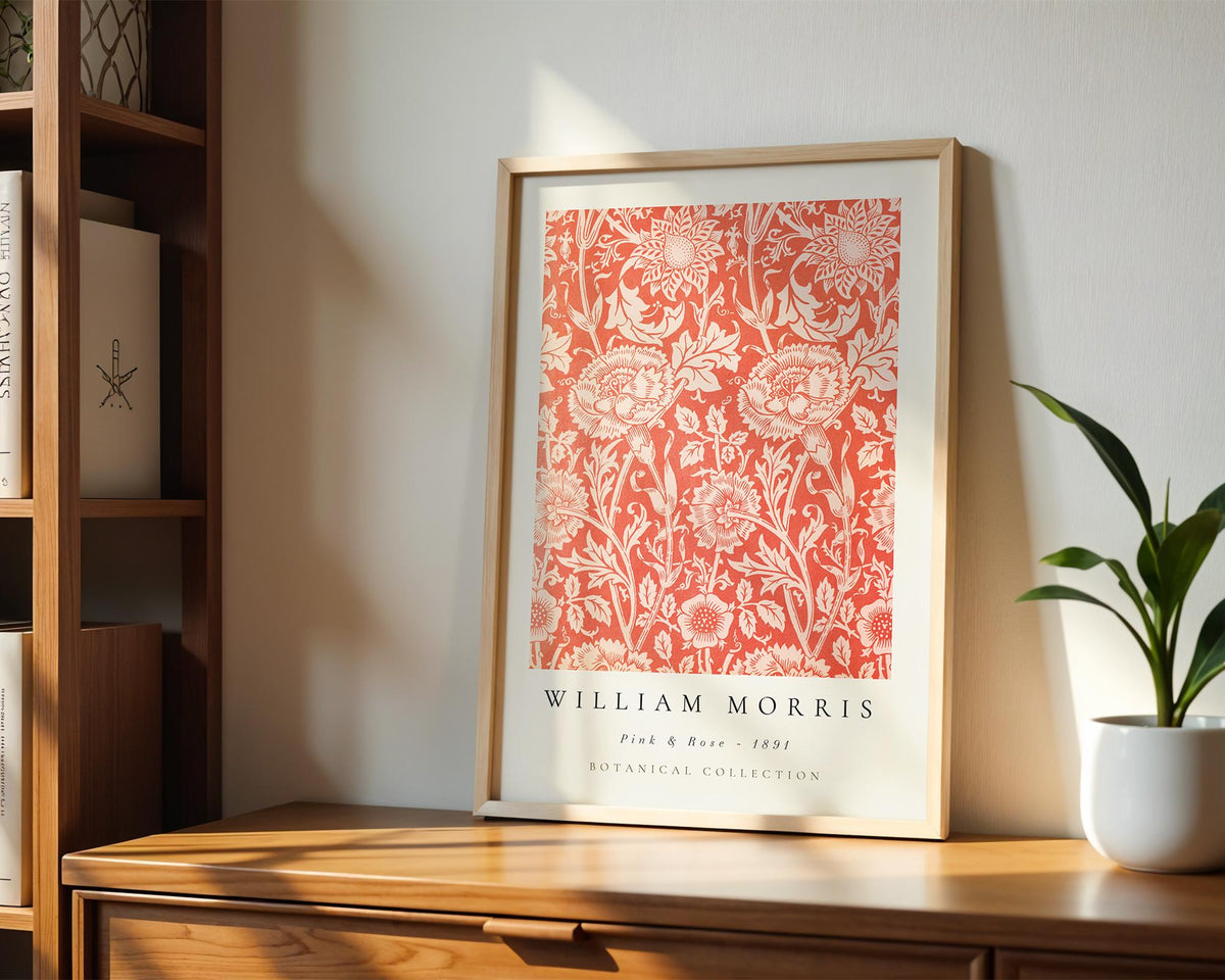 A framed print of a red floral pattern hangs on a wooden shelf, accompanied by a potted plant and a bookshelf in the background.
