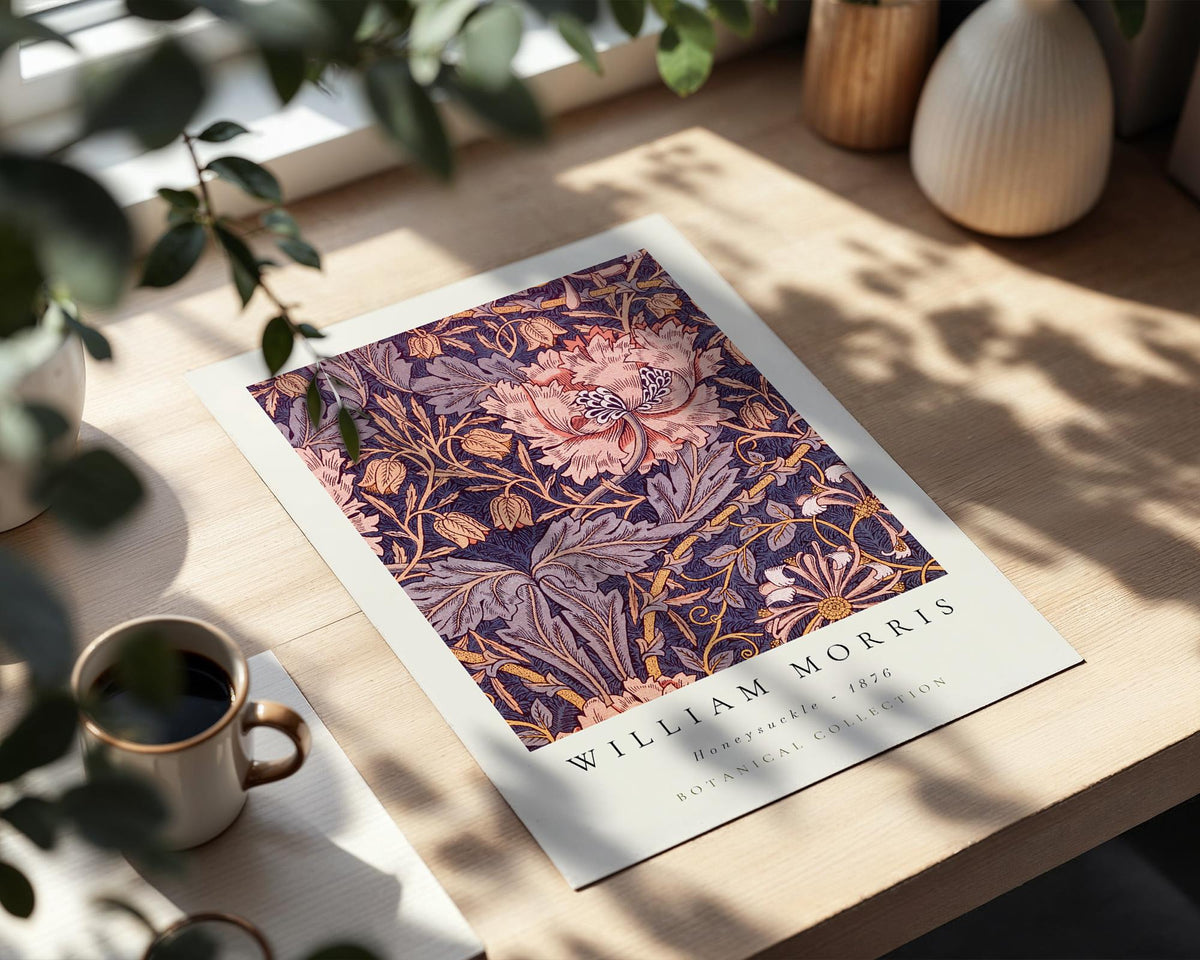 a poster of William Morris' honeymoon suite, a botanical collection, placed on a wooden table. The poster is surrounded by various decorative items, including a vase, a cup, and a potted plant.