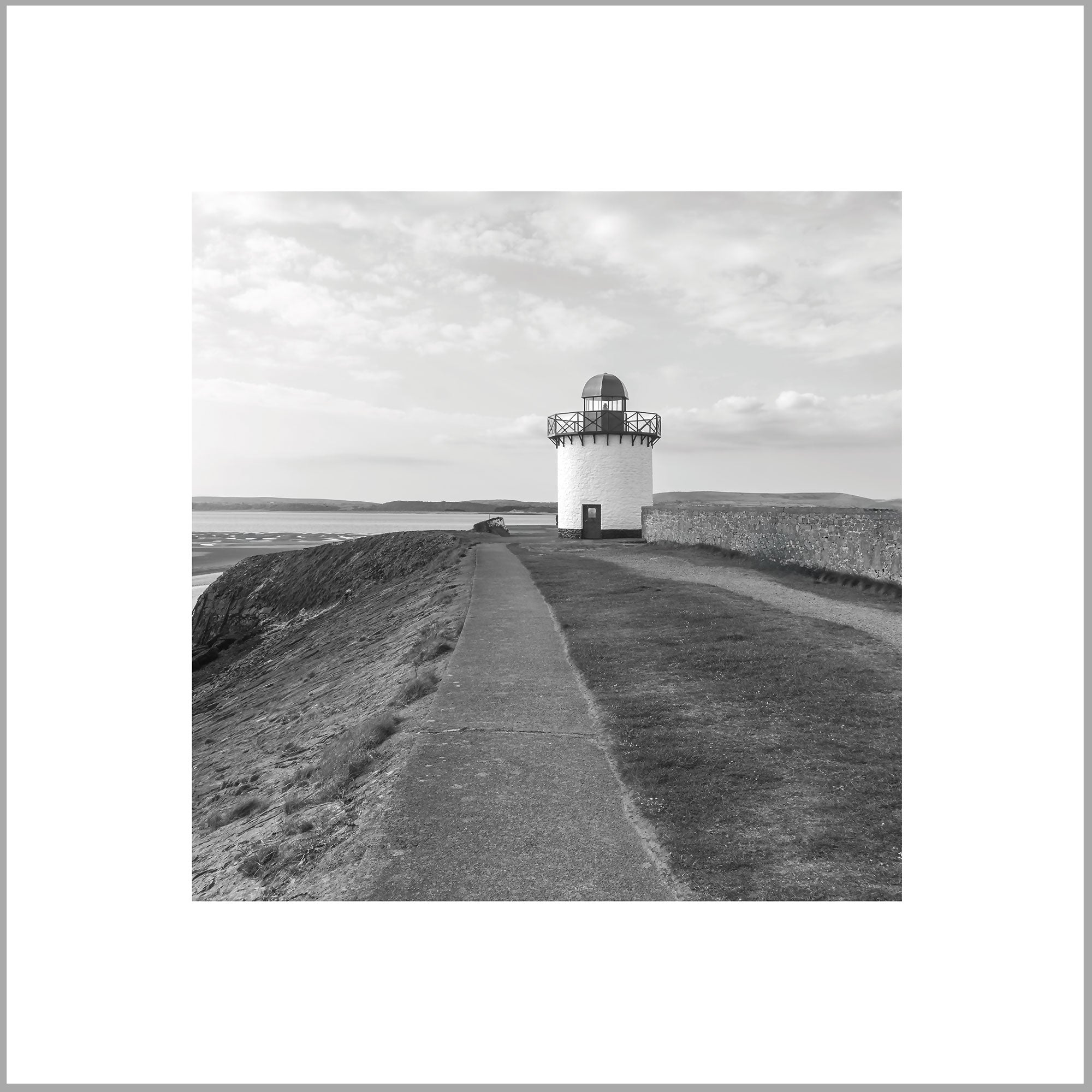 A black and white photograph of a lighthouse standing on a grassy hill, with a path leading up to it.